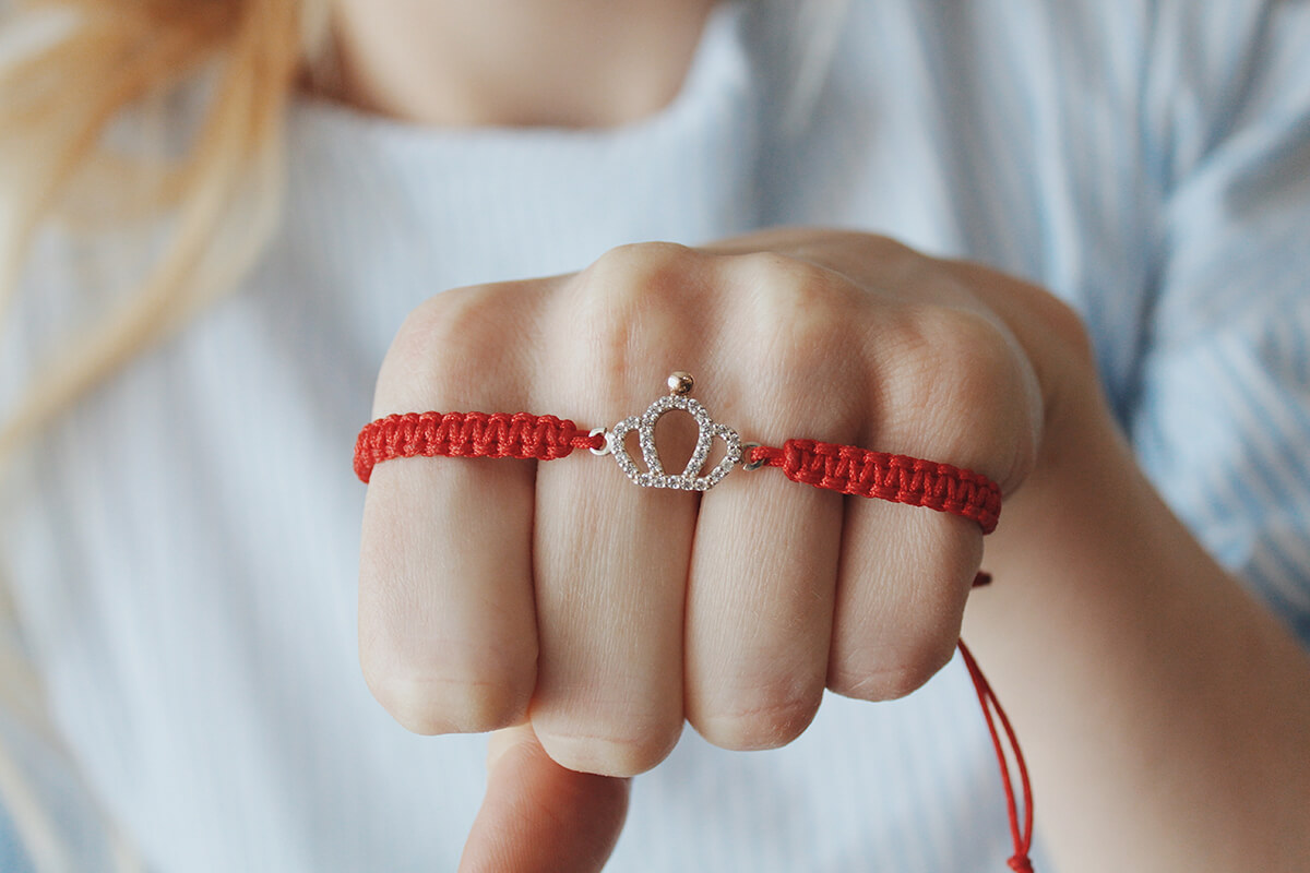 closeup shot red thread bracelet with silver crown pendant female's hand