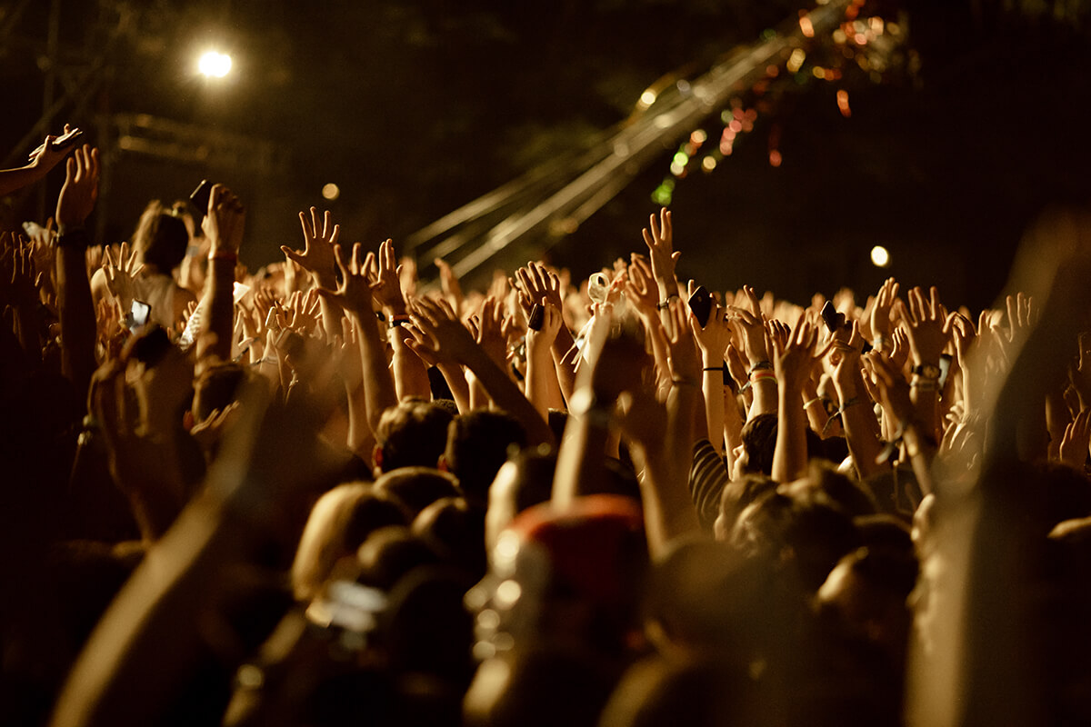 large group fans with arms raised having fun music concert night